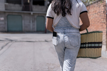 A young Hispanic woman is walking with a wicker basket and a phone in his back pocket