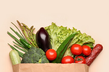 Paper bag with vegetables and sausage on beige background