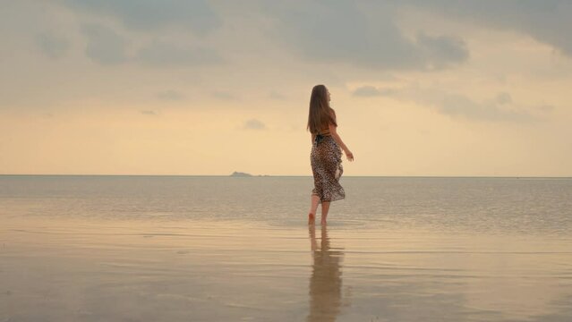 Beautiful long-haired girl twirling on the beach at sunset
