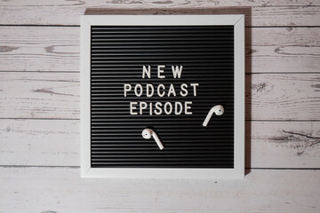 Announcement Letter board with text NEW PODCAST EPISODE on wooden table with wireless headphones....