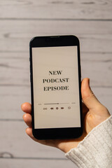 Unrecognizable woman holding mobile phone NEW PODCAST EPISODE listening website page app application with wireless headphones. Audio healing, sound therapy wellness rituals, positive mental health