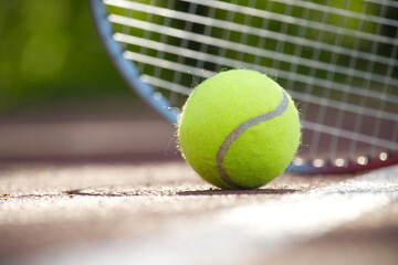 Tennis racquet and yellow tennis ball on outdoor court