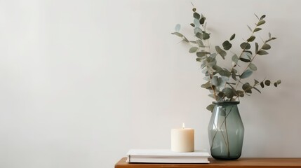 A glass vase with a eucalyptus branch sits on a table next to a candle. Generative AI