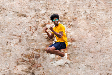 Happy young black man jumping in the air. Rustic brick and stone wall background.