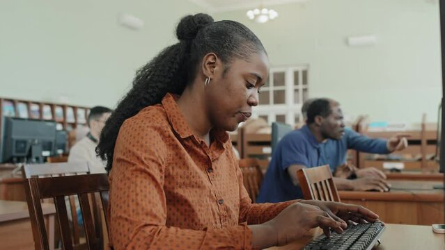 Selective focus shot of young Black migrant woman working on lesson task using desktop computer