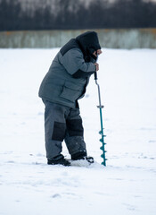 Fototapeta na wymiar A fisherman drills a hole in the ice in winter.