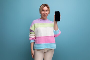 attractive blond woman in a casual look demonstrates a smartphone screen mockup on a blue background