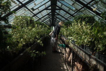 A woman bent over and sniffing the plants in the greenhouse