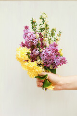 Hand holding bundle of Flowers Purple, Yellow, & White