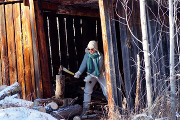 A middle-aged woman is chopping wood under a shed