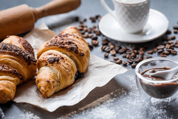 Delicious freshly baked croissants with chocolate and coffee on a dark background. French breakfast. Delicious pastries close-up. The context of a bakery with delicious bread. Confectionery products.