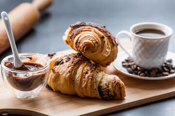 Delicious freshly baked croissants with chocolate and coffee on a dark background. French breakfast. Delicious pastries close-up. The context of a bakery with delicious bread. Confectionery products.
