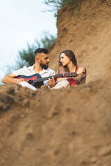Fototapeta premium A girl and a boy play the guitar in the field. A romantic date. Couple in love spending time together. The relationship of two lovers.