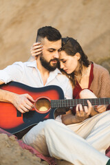 A girl and a boy play the guitar in the field. A romantic date. Couple in love spending time...