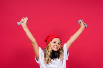 Kid girl doing fitness exercises with dumbbells on red background