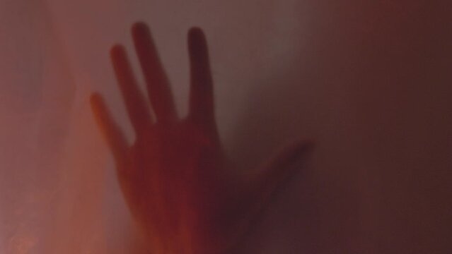 The silhouette of the killer. Bloody hand against blurred wet plastic shower curtain. Horror scene for halloween. High quality FullHD footage with slow motion