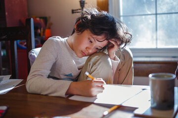 A child with head in hands focuses on schoolwork at home