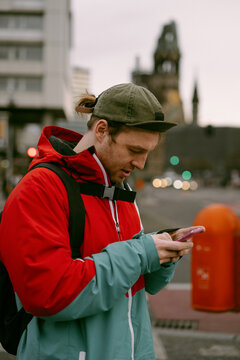 A young man tourist uses a navigator and a map on phone.