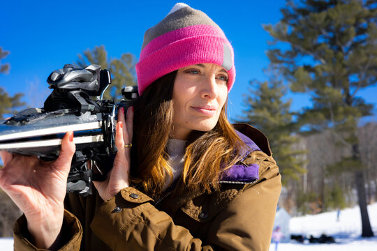 A woman carrying skis outside