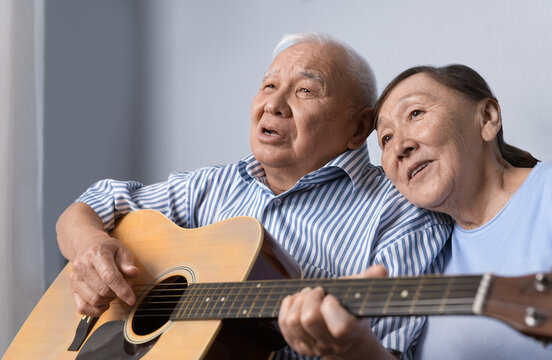 Senior man playing acoustic guitar and singing with his wife at home
