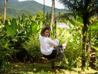 A woman smiles as she swings on a swing in the middle of the rainforest.