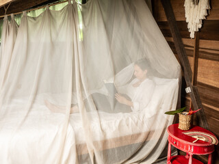 Fototapeta na wymiar Woman lying in bed reading a book and with the mosquito nets down