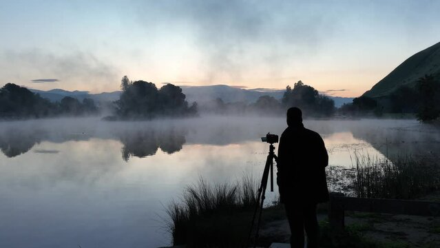 Silhouette of a photographer taking pictures of a misty lake at predawn