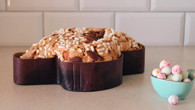  Colomba pasquale-Italian Easter cake on the kitchen table. Easter cake in the shape of a dove with almonds and orange peel. Traditional Italian pastries. paschal eggs in a bowl in the form of a rabbi