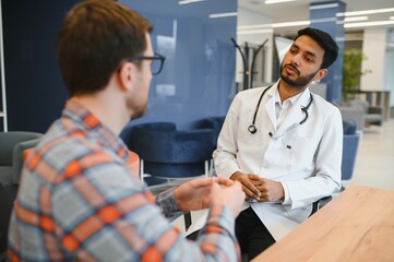 Indian doctor in white gown seeing patients in office.