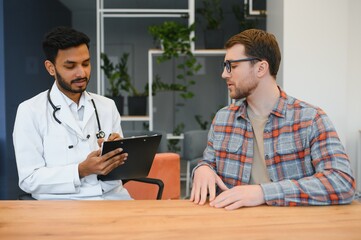 medicine, healthcare and people concept - indian doctor giving prescription to male patient at clinic