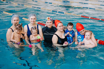 Moms and their newborns playing together with balls and pool noodles at infant swimming class