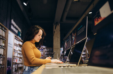 Fototapeta na wymiar Focused young woman examines laptop on display in tech store department.