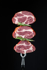 Three sliced smoked steaks or ham with rosemary on a fork. Natural product from an organic farm. Place for a recipe for a hotel on a black background.