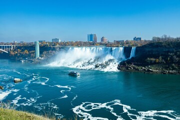 Aerial shot of Niagara Falls and a cruise ship on the Niagara River under the blue sky