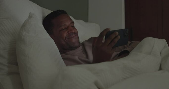 African American Male using a Smartphone in bed at nighttime
