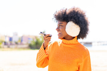 African American girl wearing winter muffs at outdoors keeping a conversation with the mobile phone