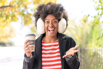 African American girl wearing winter muffs while holding a coffee at outdoors with shocked facial...