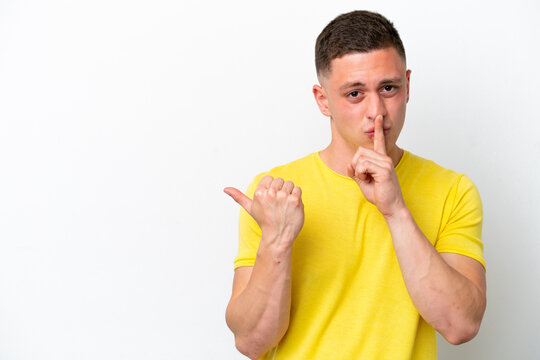 Young brazilian man isolated on white background pointing to the side and doing silence gesture