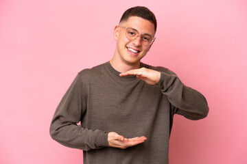Young Brazilian man isolated on pink background holding copyspace imaginary on the palm to insert...