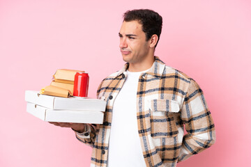 Young caucasian man holding fast food isolated on pink background suffering from backache for having made an effort