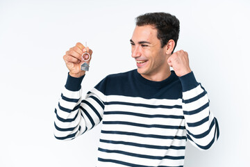 Fototapeta premium Young caucasian man holding home keys isolated on white background celebrating a victory