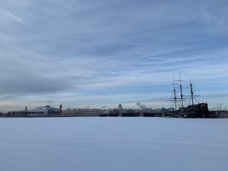 View from the Mytninskaya embankment to the ice-covered Neva, the Spit of Vasilevsky Island, the Rostral columns and the ship. Against the background of the sky with beautiful clouds in St. Petersburg