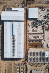 Fototapeta na wymiar Prefabricated industrial buildings at construction site. Concrete foundations and metal frameworks of warehouses under construction. Top down aerial view
