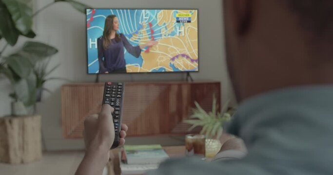 African American Male at Home Watching Weather on Television and holding Remote Control on Sofa
