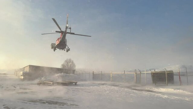 Medium shot of a helicopter on a portable helipad taking off with snow blowing around from the prop wash on clear winters day