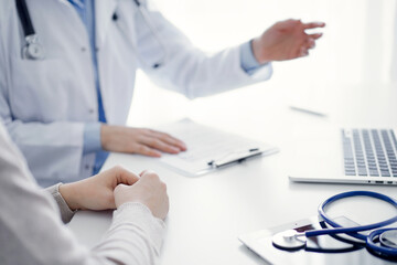 Doctor and patient discussing current health questions while sitting at the table in clinic office, only hands closeup. Medicine concept