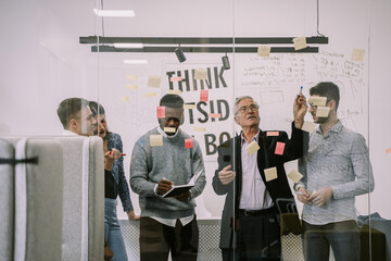 Diverse group of creative people writing on glass wall at the office