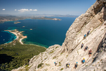 foto panoramica di una costa della Sardegna mentre un gruppo di escursionisti compie una ferrata...