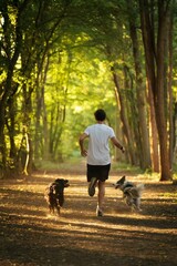 Vertical shot of a male running in a park with two Australian shepherds