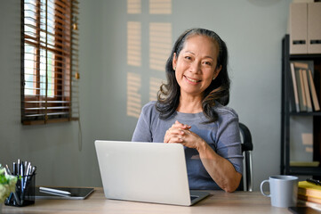 Successful Asian-aged businesswoman sits at her desk in her modern office.